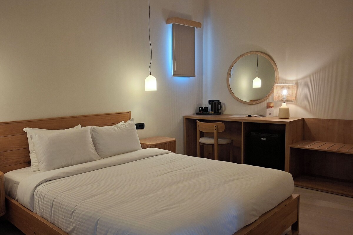 A hotel room with a bed, bedside tables, a desk with a chair, a mirror, and a lamp.