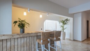 A reception area with a wooden counter, two wicker bar stools, and potted plants. - Casa Frati Suites & Villas (Santorini)