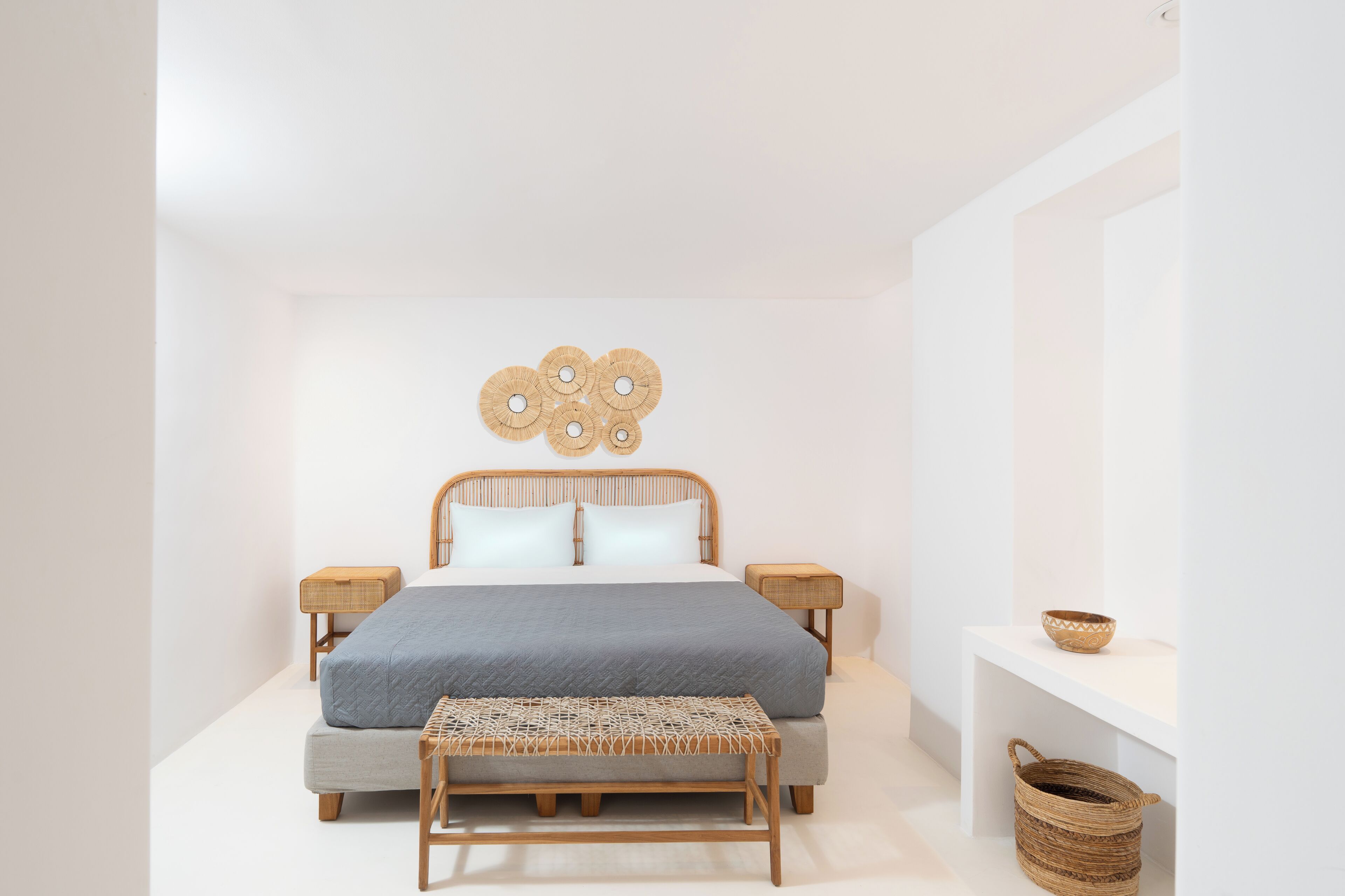 Un dormitorio minimalista con cama, mesitas de noche, un banco y estante de pared.