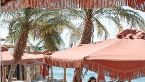 A beachside lounge area with sun loungers and palm trees. - Casa Frati Suites & Villas (Santorini)