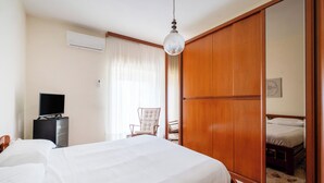A hotel room with a large bed, a television on a stand, a chair, a wardrobe, and a mirror.