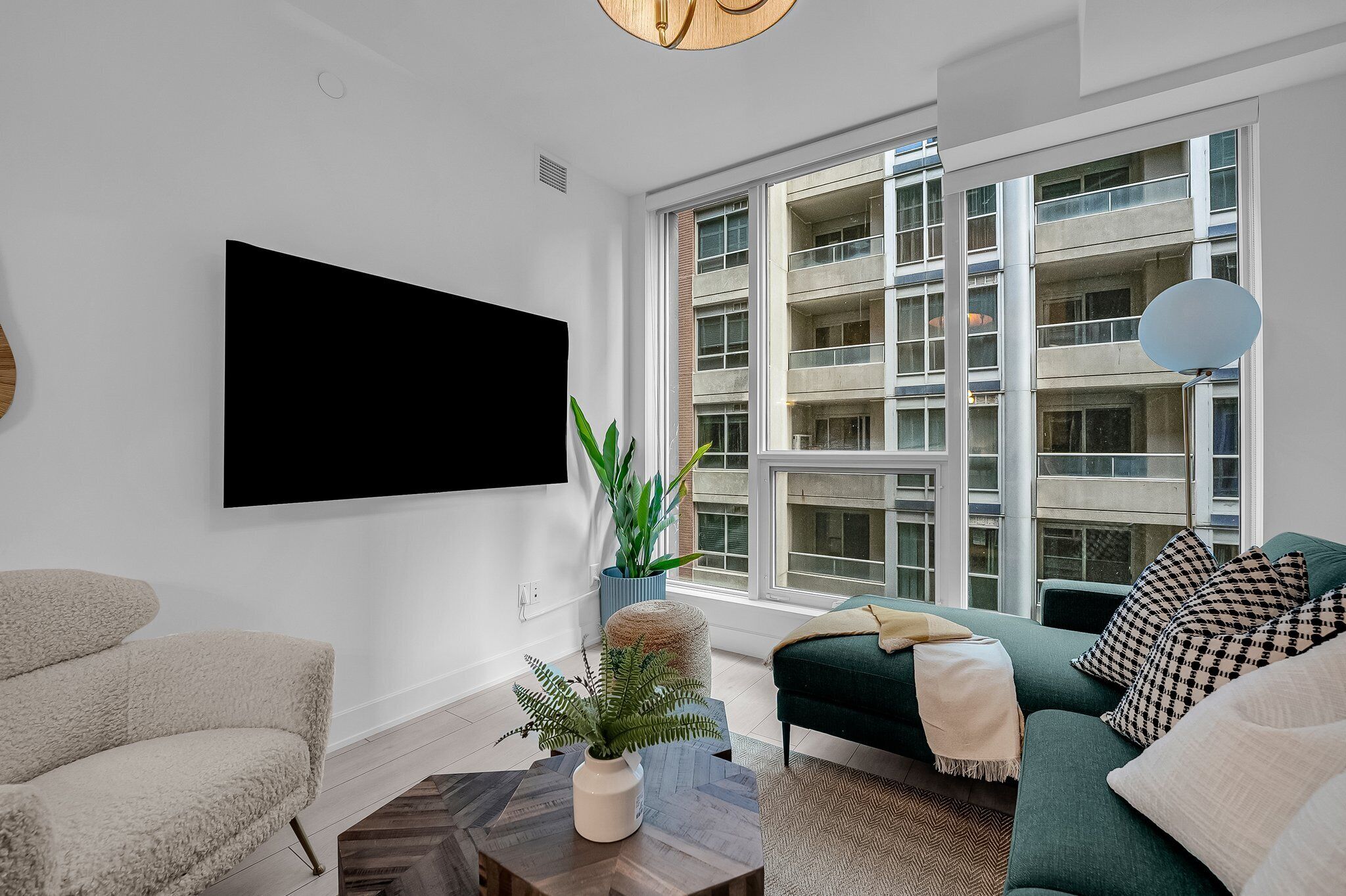 A modern living room with a large TV, a green sofa, a beige armchair, and a potted plant.