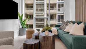 A modern living room with a green sofa, a coffee table, and a large window with a view of a building. - The Aurelien Luxe Collection (Toronto)
