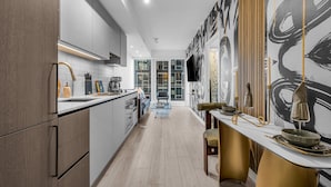A modern kitchen with a long counter, a dining area with a table and chairs, and a large abstract mural on the wall. - The Aurelien Luxe Collection (Toronto)