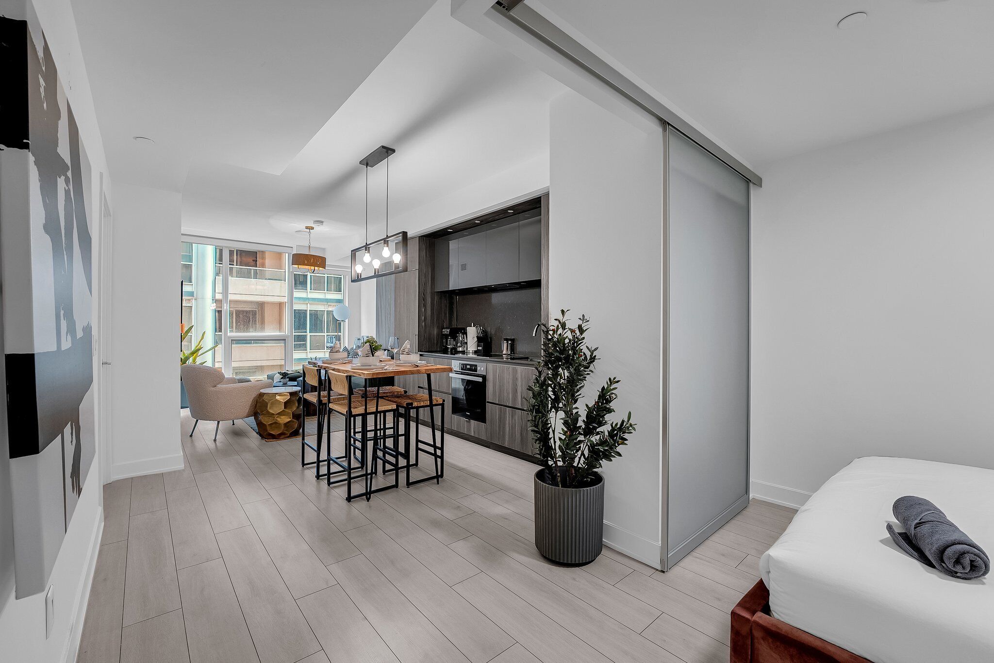 Un apartament modern amb zona de menjador, cuina i un llit amb una tovallola enrotllada.