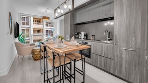 A modern kitchen with grey cabinetry, a wooden dining table set with plates and cutlery, and a pendant light above. - The Aurelien Luxe Collection (Toronto)