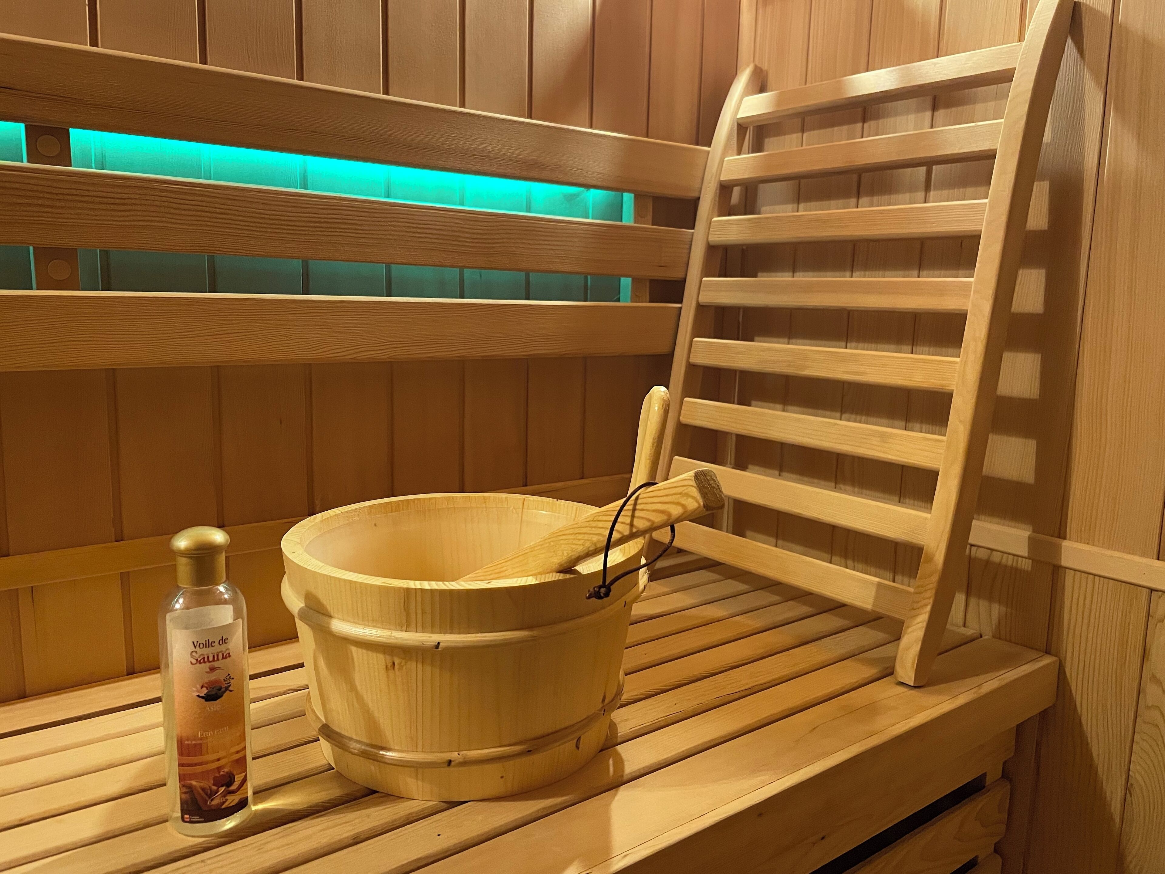Een houten sauna bank met een houten emmer en een fles lotion.