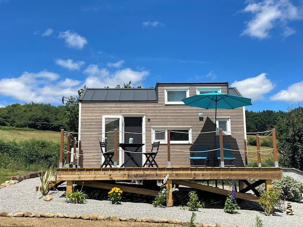 A two-story wooden cabin with a deck, outdoor seating, and a large umbrella. - La Samorienne Tiny House, with a private spa and sauna. (Réjaumont)