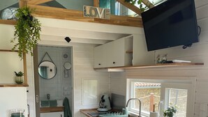 A compact kitchen with white cabinetry, a wooden countertop, a built-in TV, and a small window. - Tiny House La Samorienne, with private spa and sauna. (Réjaumont)