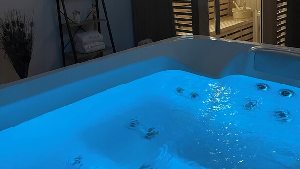 A spa area with a hot tub, wooden walls, and a small entrance to a sauna. - Tiny House La Samorienne, with private spa and sauna. (Réjaumont)