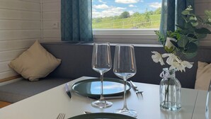 A dining area with a table set for two, a window with curtains, and a view of the outdoors. - Tiny House La Samorienne, with private spa and sauna. (Réjaumont)