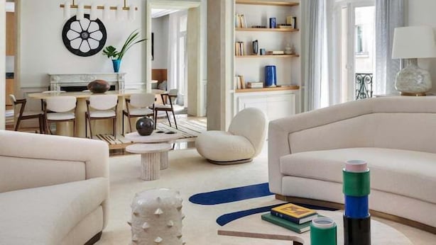 En moderne stue med et rundt sofabord, to sofaer, et spiseområde med en lysekrone og en reol.