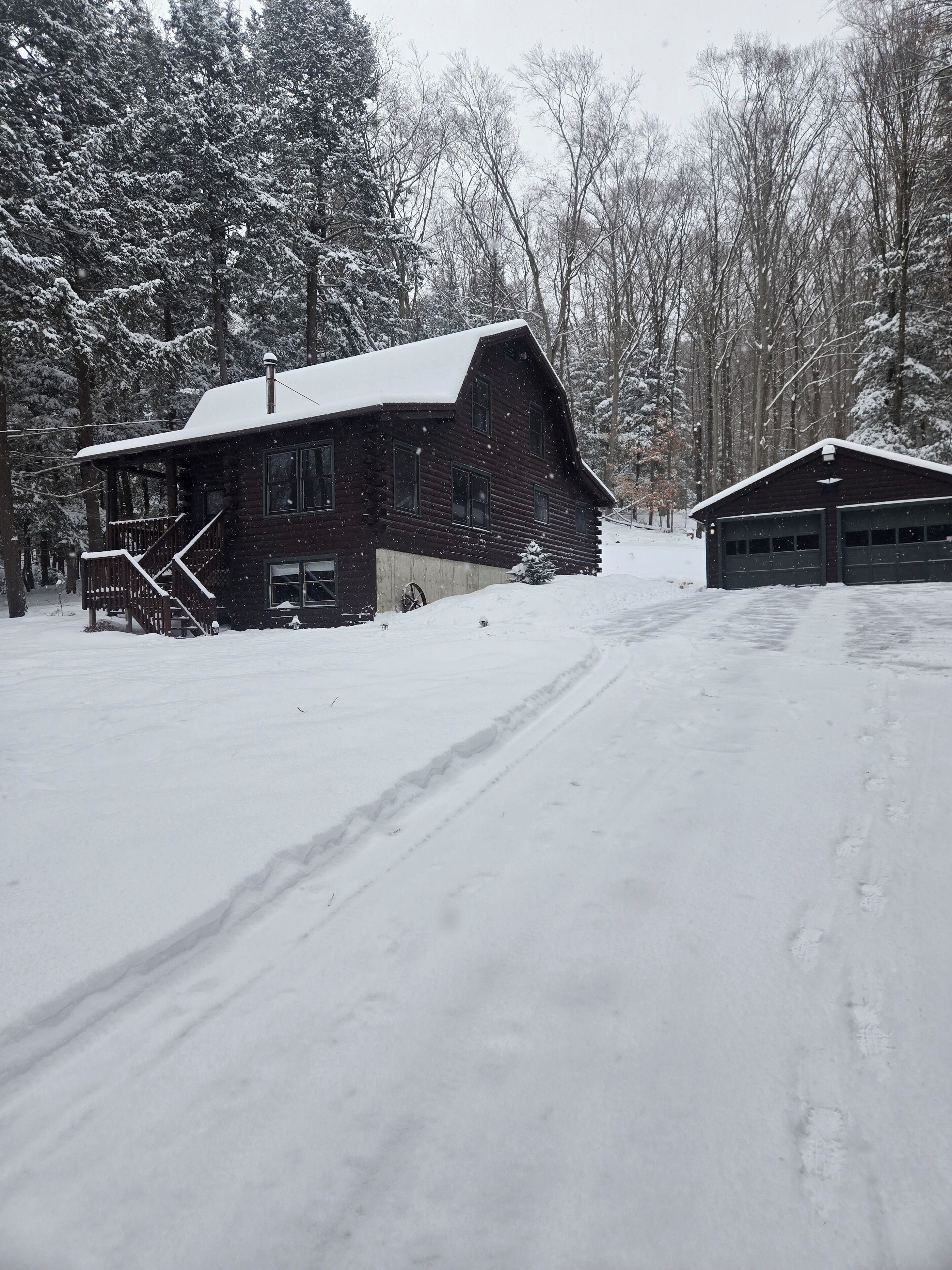 Une cabane en bois rustique, avec un toit enneigé, une véranda et un garage.