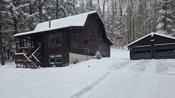 Une cabane en bois rustique, avec un toit enneigé, une véranda et un garage.
