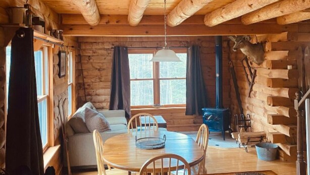 A cozy cabin interior with a wooden dining table, chairs, a sofa, and a kettle on the counter. - Cozy Fishing and Get-A-Way Cabin minutes from Lake George (Kattskill Bay)