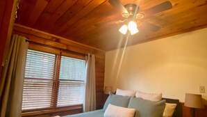 A wooden-paneled room with a bed, a ceiling fan, and a window with blinds. - Cozy Fishing and Get-A-Way Cabin minutes from Lake George (Kattskill Bay)