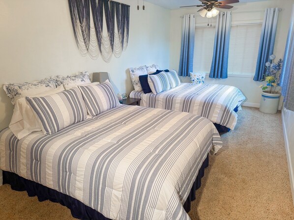 A bedroom with two beds, a ceiling fan, and a window with curtains.