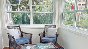 Un solárium con muebles de mimbre, una mesa de vidrio y un tapiz azul estampado.