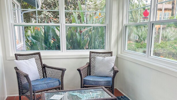 Un solárium con muebles de mimbre, una mesa de vidrio y un tapiz azul estampado.