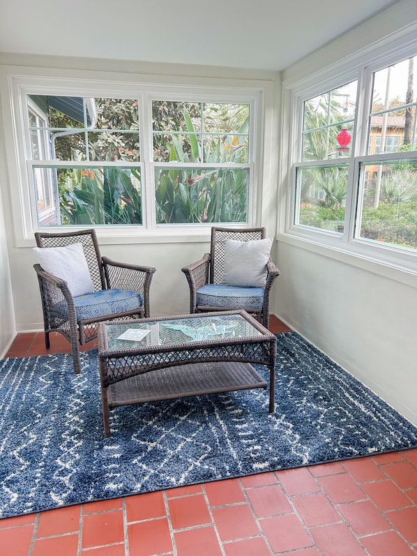 Une véranda meublée de meubles en osier, avec une table en verre et un tapis bleu à motifs.