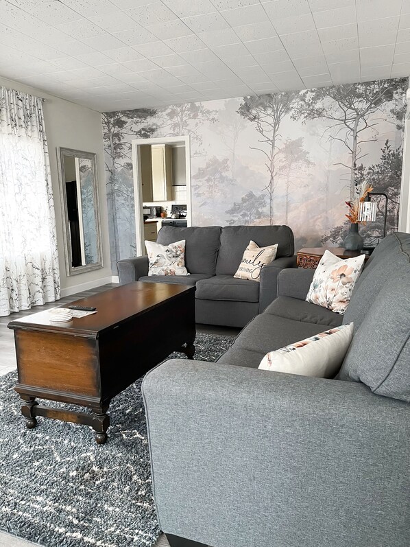 Ein Wohnzimmer mit einem grauen Sofa, einem Holztisch und einem gemusterten Teppich.
