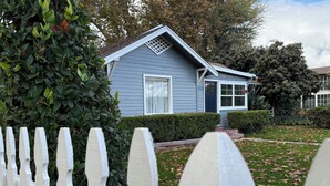Una casa residencial con fachada gris, cerca viva blanca y un césped cuidado con hojas caídas.