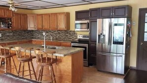A kitchen with a large island, bar stools, wooden cabinets, a stainless steel refrigerator, and a microwave. - Private Lake with 180° views (Uxbridge)