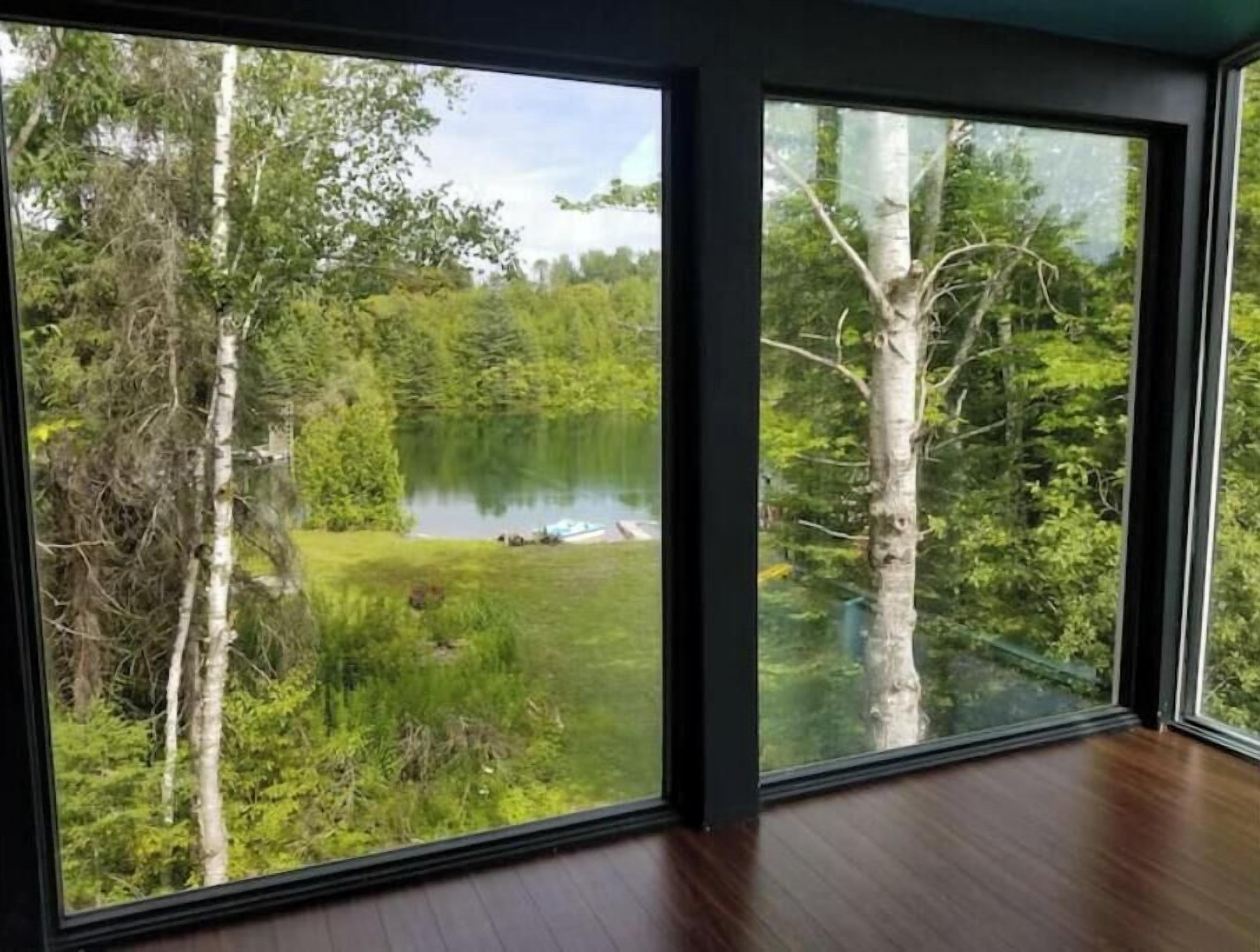 Quarto com grandes janelas proporcionando vista para um lago rodeado por árvores.