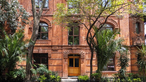 A red brick building with a central entrance, surrounded by lush greenery and trees. - New Apartment City Oasis In Roma Norte (Mexico City)