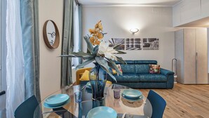 A modern living room with a blue sofa, a glass dining table with blue chairs, and a decorative plant.