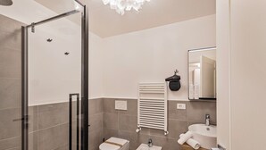A modern bathroom with a glass shower enclosure, a bidet, a toilet, and a sink with a mirror above it.