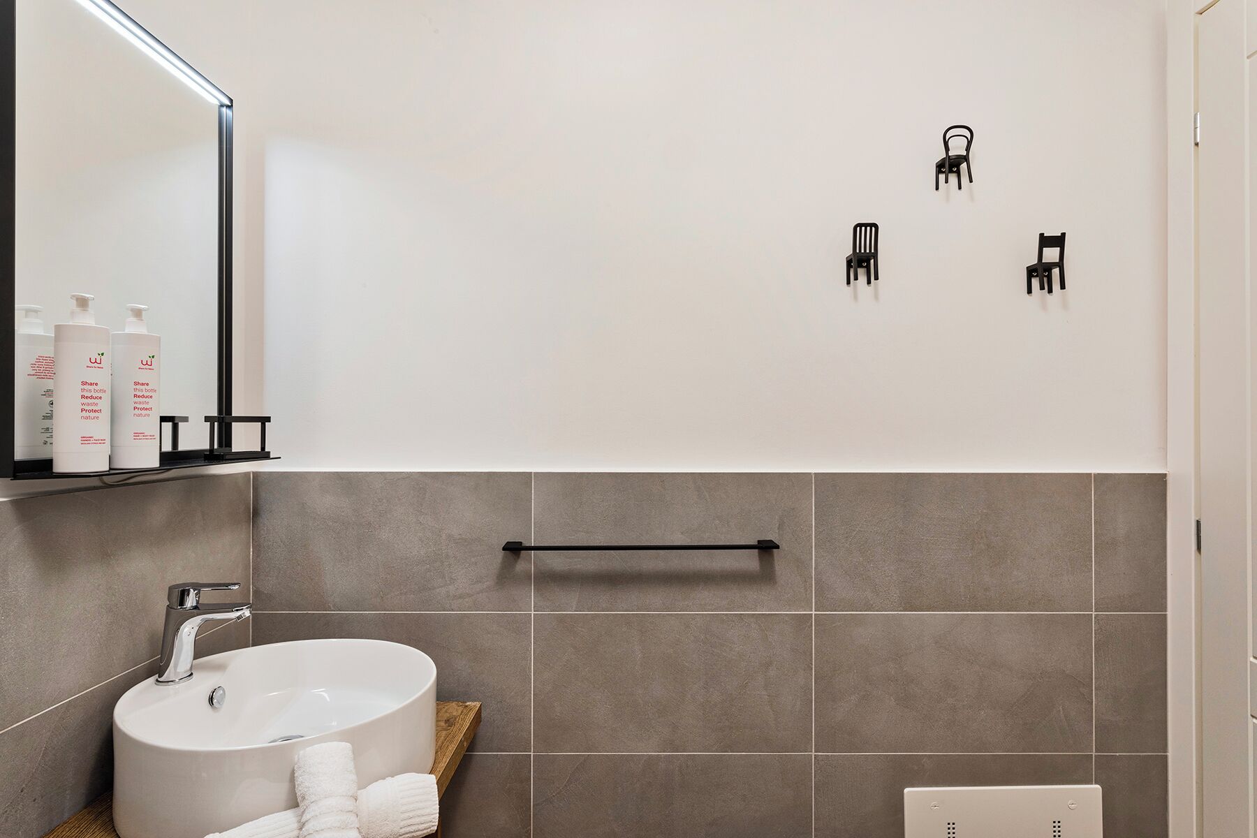 A modern bathroom with a white sink, a mirror, and three black wall-mounted chairs.