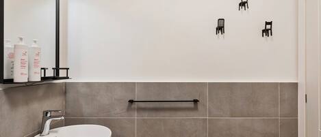 A modern bathroom with a white sink, a mirror, and three black wall-mounted chairs.