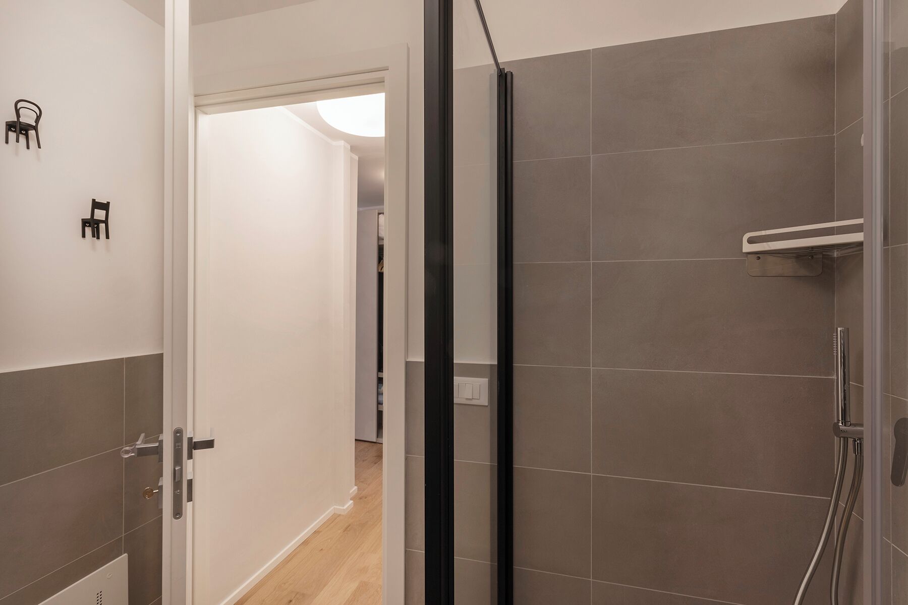 A modern bathroom with a glass shower enclosure, tiled walls, and a visible toilet in the adjacent room.