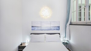 A bedroom with a bed, a wall-mounted light, a painting, and a window with curtains.