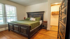 Un dormitorio con una cama de madera, una mesita de noche, un aparador y una ventana con persianas.