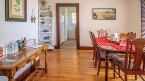 Un comedor con una mesa y sillas de madera, un camino de mesa rojo y una estantería con un letrero que dice 'FARMHOUSE'.