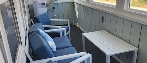 Uma sala de sol com vista para o exterior, com área de estar incluindo cadeiras estofadas azuis e uma mesa pequena.