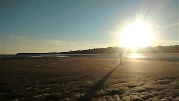 A beach with footprints leading towards the water, a clear sky, and the sun low on the horizon.