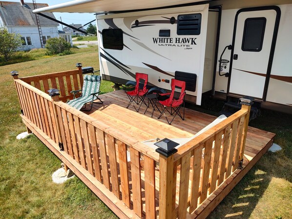 A recreational vehicle with a wooden deck, two folding chairs, and a grill area.