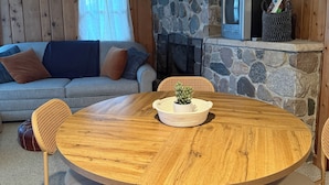 Un salon chaleureux avec une cheminée en pierre, un téléviseur et une table ronde en bois, entourée de chaises.