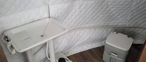 A corner of a room with a white quilted wall, a small white sink with a mirror, and a white toilet.