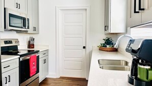 Una cocina con gabinetes blancos, microondas, horno, cafetera y lavamanos.