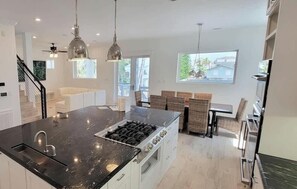 Cozinha moderna com ilha central, eletrodomésticos de aço inoxidável, iluminação pendente e vista para o exterior.