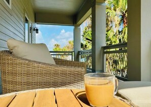 Ein Korbstuhl mit Kissen, ein Holztisch und ein Glas Orangensaft auf einem Balkon mit Blick auf Palmen.