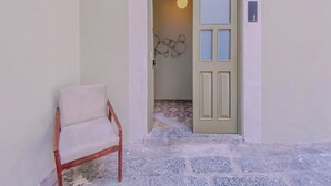 A narrow entrance with a wooden chair outside, a door with a light fixture inside, and a wall-mounted light fixture above the door. - Beautiful double suite in an old house with contemporary restoration.  (Heroica Puebla de Zaragoza)