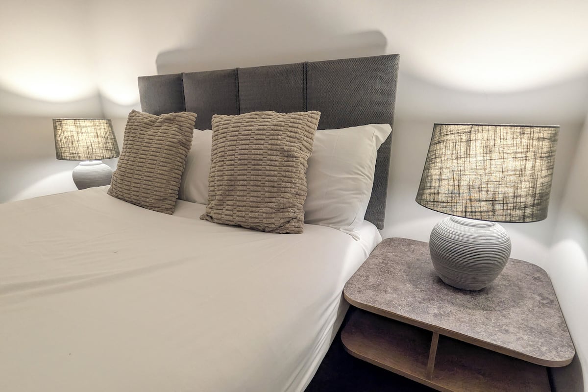 A neatly made bed with a headboard, two bedside tables with lamps, and a decorative vase on one table.