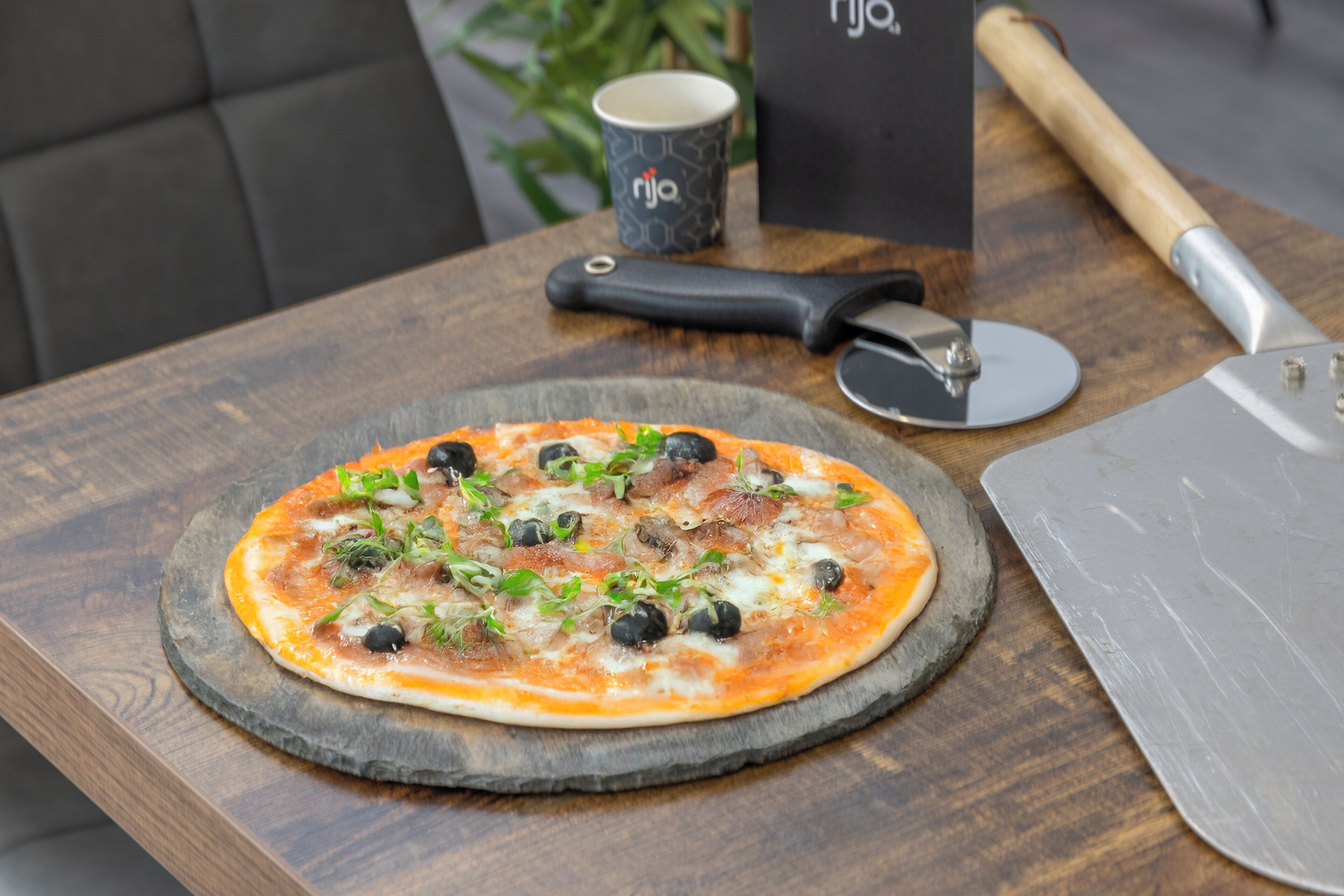 Une pizza sur une planche en bois, avec un coupe-pizza et une tasse en arrière-plan.