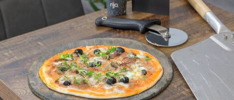 Une pizza sur une planche en bois, avec un coupe-pizza et une tasse en arrière-plan.