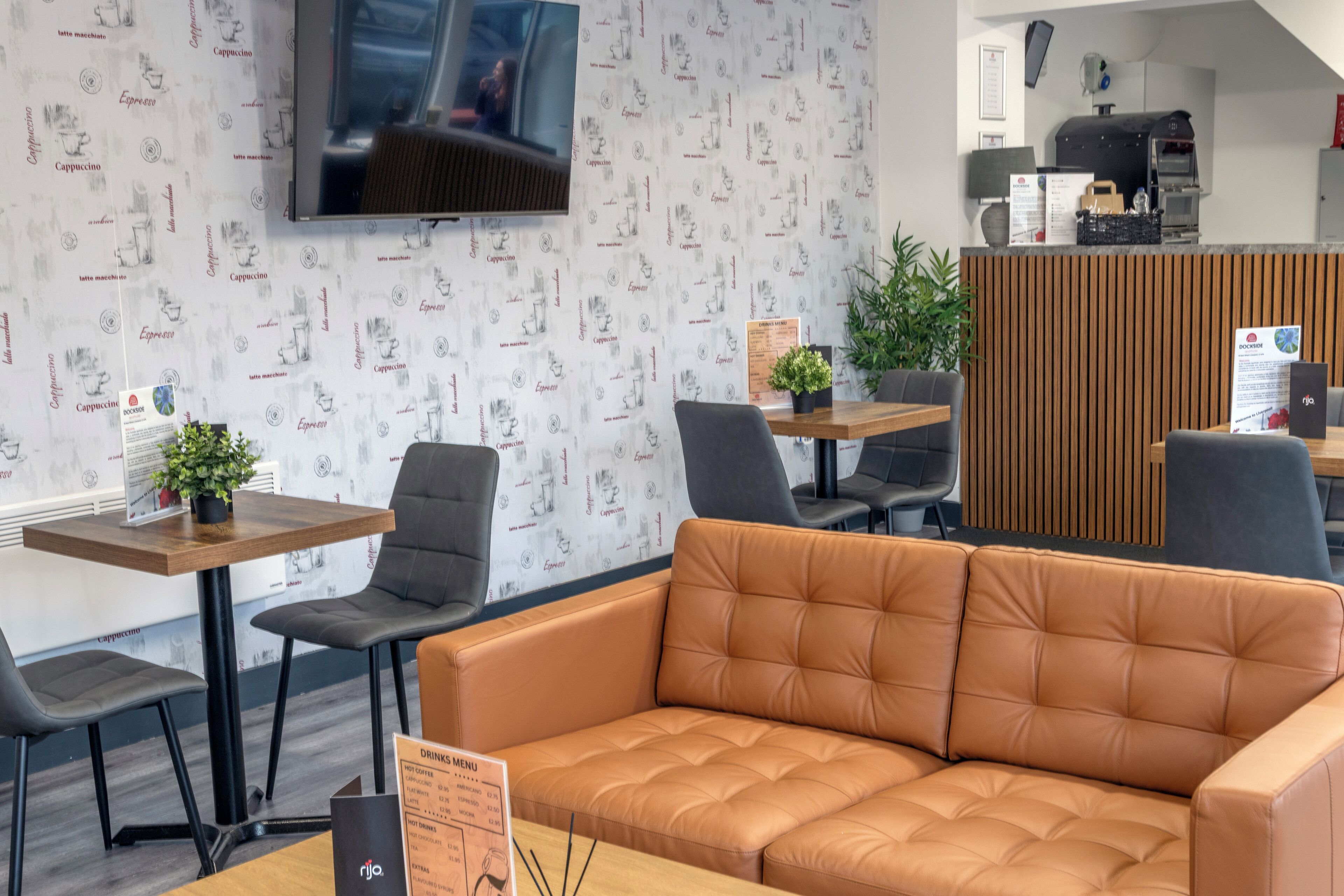 A modern cafe with a wooden counter, black chairs, a leather sofa, and a menu stand.